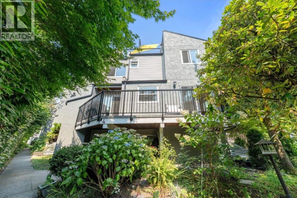 Rear exterior view of the townhouse showing multiple balconies, grey siding, and surrounding lush green trees and foliage. - 4 230 W 16th Street, North Vancouver