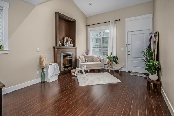Living area with a fireplace, sofa, rug, and plants, with a white door. - 4 30748 Cardinal Avenue, Abbotsford