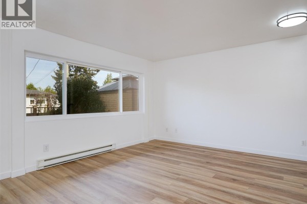 Living room with light wood laminate flooring, white walls, a door, and a large sliding window. - 4 740 Wilson St, Victoria
