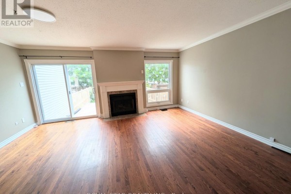 Living room with dark wood floors, a white fireplace, and large windows overlooking the backyard. - 4 Alfa Street, Ottawa