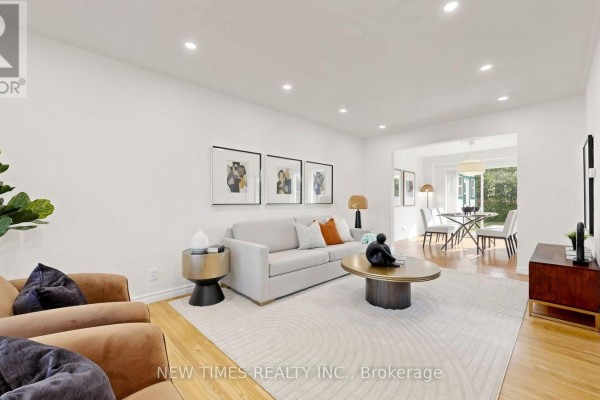 Living room with a beige sofa, round coffee table, and a view into a dining area with a table and chairs. - 4 Ashstead Place, Toronto