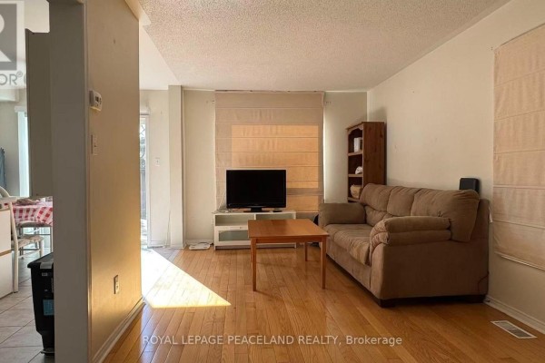 Living room with hardwood floors, a brown sofa, coffee table, television, and a bookshelf. - 4 Attilio Street, Markham
