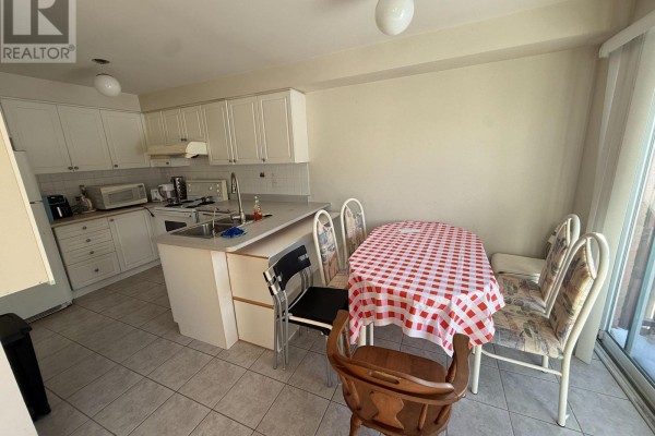 Kitchen with white cabinets, a sink, appliances, and a dining area with a checkered tablecloth. - 4 Attilio Street, Markham