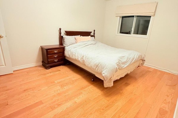 Bedroom with light wood floors, a wooden nightstand, and a queen-sized bed with grey bedding. - 4 Attilio Street, Markham