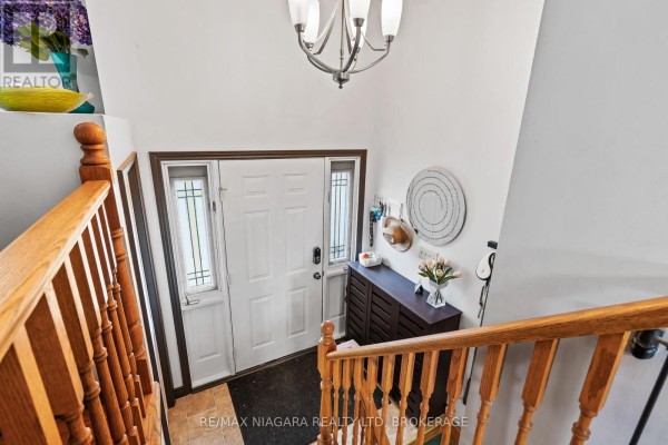 View of a home's entryway with a white door, wooden staircase, and dark wood cabinet. - 4 Barbara Street, West Lincoln