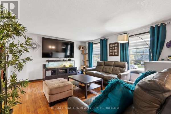 Living room with brown leather sofas, teal curtains, a large television, and hardwood floors. - 4 Barbara Street, West Lincoln