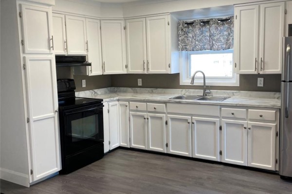 A modern kitchen with white cabinets, black appliances, and grey laminate flooring. - 4 Bay Street, Little Burnt Bay