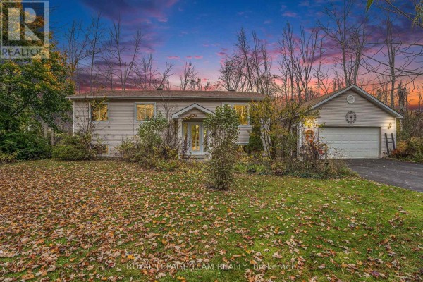 Front exterior of a white bungalow with a detached garage at dusk, autumn leaves on the lawn. - 4 Black Walnut Road, North Grenville