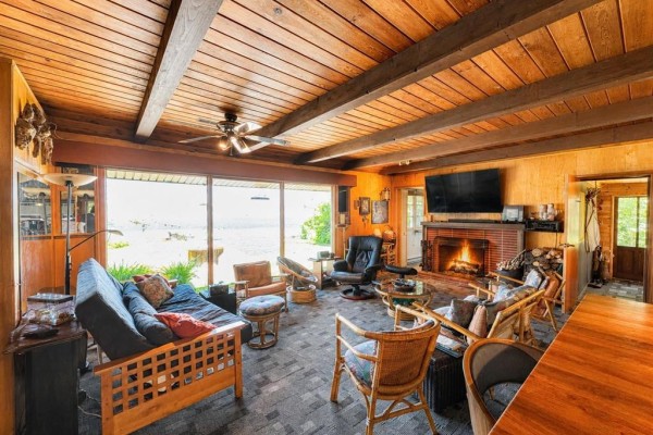Cozy living room with a fireplace, large windows overlooking the water, and wood-paneled ceiling. - 4 Block 4 Road, Otterfalls
