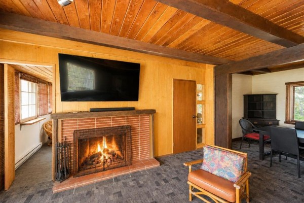 Living room fireplace with a mounted television above, brick surround, and wood-paneled walls. - 4 Block 4 Road, Otterfalls