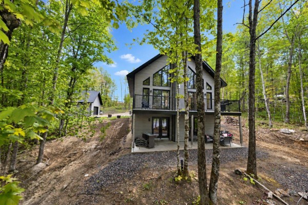 Exterior view of a grey house with a detached garage and gravel driveway. - 4 Ch. Des Contes, Notre Dame De Pontmain