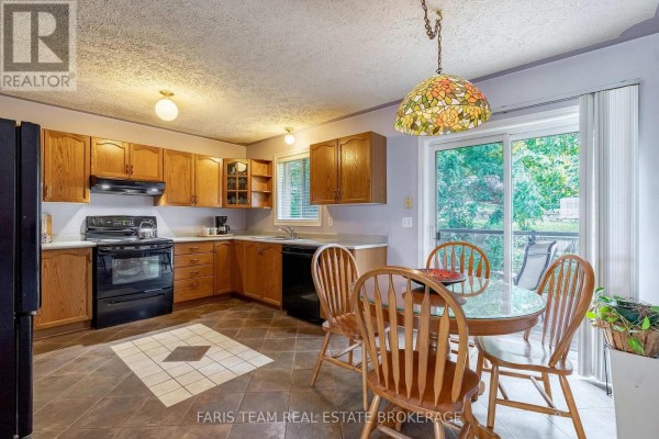 Kitchen with wood cabinets, black appliances, a circular dining table with four wooden chairs, and a sliding glass door. - 4 Charles Street, Penetanguishene