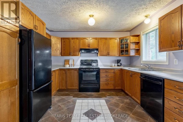 U-shaped kitchen featuring light wood cabinets, black appliances, a tiled floor, and a window above the sink. - 4 Charles Street, Penetanguishene