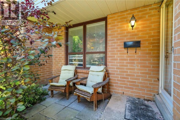Covered front porch with two wooden chairs, stone patio, and brick wall. - 4 Eileen Street, Waterdown