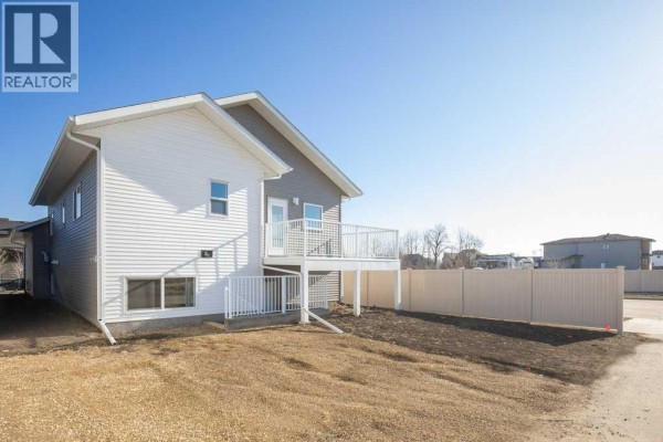 View of the backyard with a white deck and fence, adjacent to a paved pathway. - 4 Emmett Crescent, Red Deer