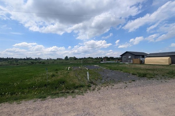 Vacant lot with grass, gravel driveway, and houses nearby under a partly cloudy sky. - 4 Falcon West Drive, Falcon Lake