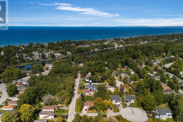 Aerial view of a suburban neighborhood with dense green trees and a distant view of Lake Huron. - 4 Fatima Court, Wasaga Beach