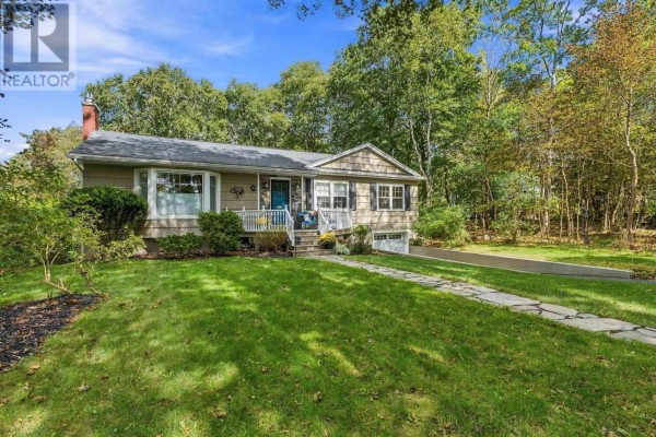 A wider angle of the beige bungalow exterior showing the front lawn, walkway, and surrounding trees. - 4 Fleming Drive, Halifax