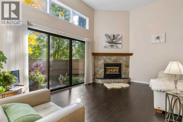 Living room fireplace with stone surround and wood mantle, next to sliding glass doors. - 4 Glamis Gardens Sw, Calgary