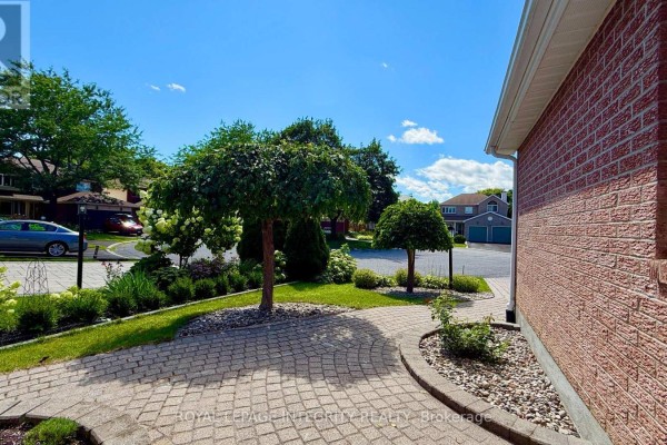 View of a paved driveway curving towards the house with manicured trees and shrubs. - 4 Glenarden Court, Ottawa