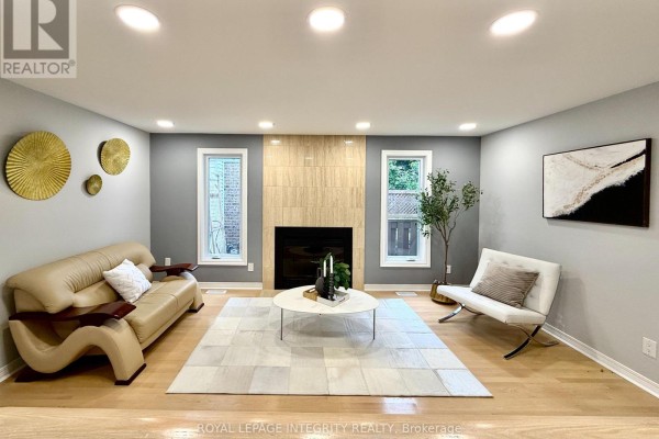 Living room with a fireplace, light wood floors, and grey walls with art. - 4 Glenarden Court, Ottawa