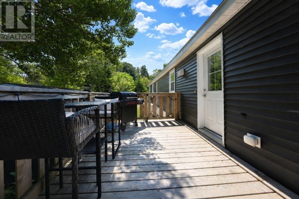 Wooden deck with patio furniture and a grill, attached to the side of a dark grey house. - 4 Kellys Lane, Ingonish