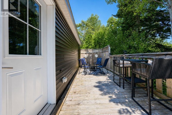 Deck space with seating and tables, looking towards a white door and the side of a dark grey house. - 4 Kellys Lane, Ingonish