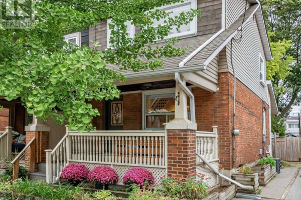 Side view of a brick house exterior with a covered porch and green foliage. - 4 Kenrae Road, Toronto