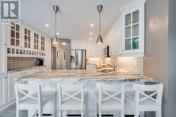 Kitchen island with granite countertop and four white stools, facing white cabinetry and appliances. - 4 Milgate Place, Aurora