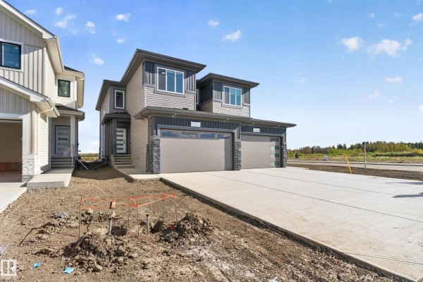 Duplex exterior with grey siding, dark trim, and double garages on a sunny day. - 4 Parker Ln, Spruce Grove
