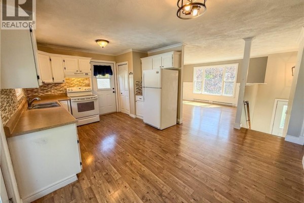 Interior view of a bright kitchen with white cabinets and wood floors, open to a living area. - 4 Phillips Street, Sussex Corner