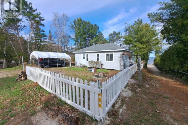 Side exterior view of a light blue cottage with a white picket fence and path to the water. - 4 Pinewood Drive, Tiny
