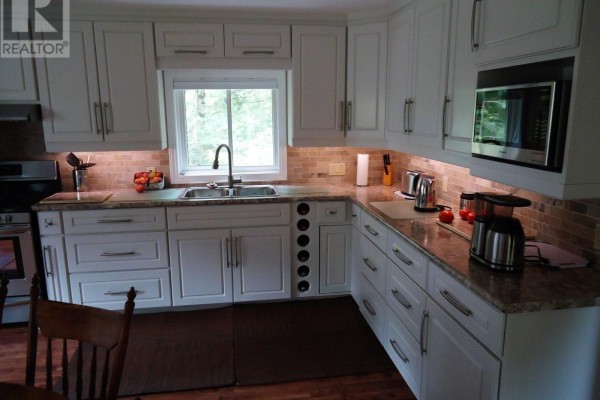 L-shaped kitchen with white cabinetry, granite countertops, tile backsplash, and a sink overlooking trees. - 4 Pinewood Drive, Tiny