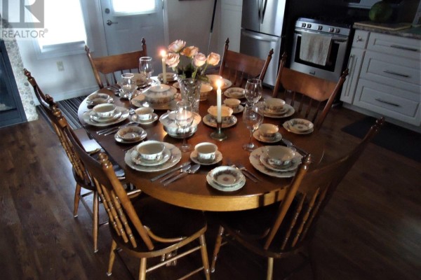 Round wooden dining table set for a formal meal with chairs in a dining area. - 4 Pinewood Drive, Tiny
