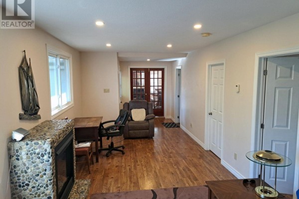Living room with hardwood floors, a stone fireplace, a recliner, and double doors leading outside. - 4 Pinewood Drive, Tiny