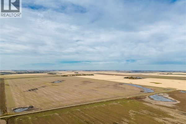 Expansive agricultural land with fields, water puddles, and distant farm buildings under a cloudy sky. - 4 Quarters Development Land Near Regina, Sherwood Rm No  159