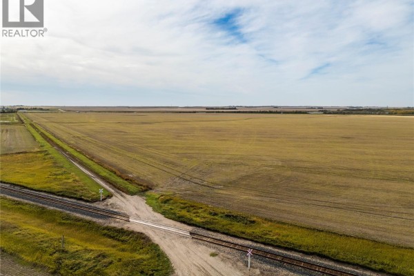 Overhead view of a rural landscape featuring train tracks crossing a road adjacent to large, empty fields. - 4 Quarters Development Land Near Regina, Sherwood Rm No  159
