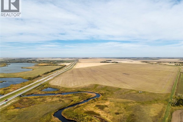 Wide aerial shot showing a highway bordering cultivated fields and natural water channels under a blue sky. - 4 Quarters Development Land Near Regina, Sherwood Rm No  159