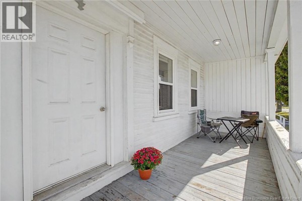 Covered front porch with white wooden floor and railing, a table, and chairs. - 4 River Street, Fredericton