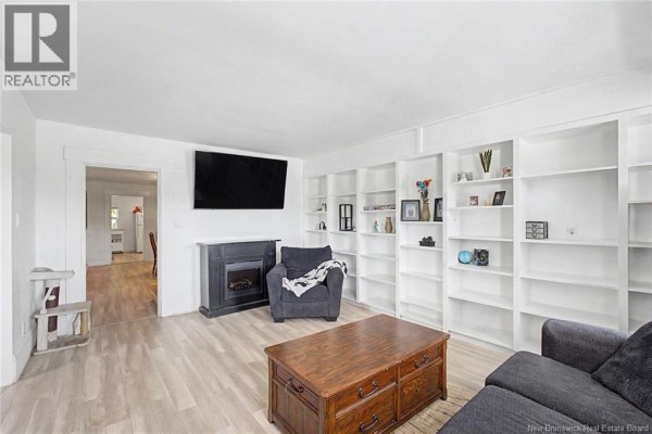 Living room with light wood floors, a fireplace, built-in white bookshelves, and a TV. - 4 River Street, Fredericton