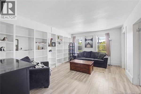Living room with white built-in bookshelves, dark sofa, coffee table, and windows showing greenery. - 4 River Street, Fredericton