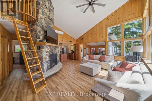 Living room with a large stone fireplace, wooden walls, and a ladder leading to a loft. - 4 Stackwall Lane, Greater Madawaska