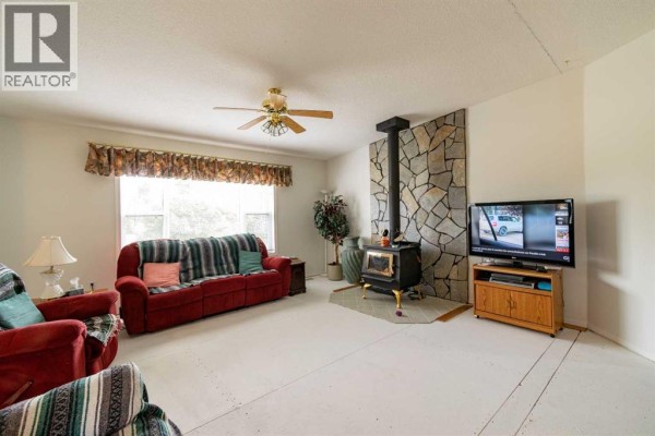 Living room with a red sofa, wood stove on a stone hearth, and television. - 4 Trestle Close, Rural Stettler No  6, County Of