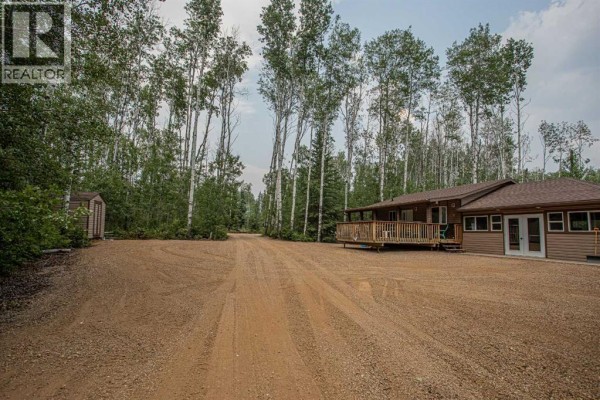 A gravel driveway leads past a detached shed towards a single-story house with a wooden deck. - 40 & 41 Tugate Drive, Rural Mackenzie County