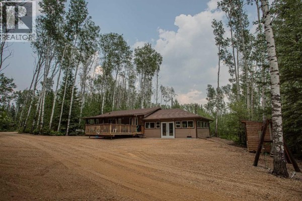 Exterior view of a single-story house with a wooden deck, surrounded by birch and evergreen trees. - 40 & 41 Tugate Drive, Rural Mackenzie County