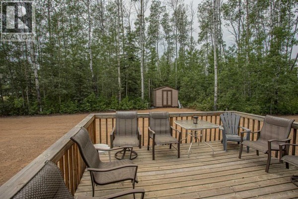 A wooden deck with several chairs and a glass-top table, overlooking a wooded area and shed. - 40 & 41 Tugate Drive, Rural Mackenzie County