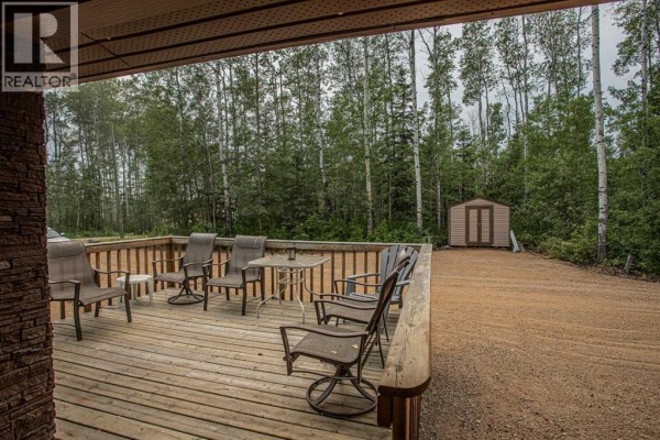 View from under a covered porch onto a wooden deck with outdoor seating and surrounding trees. - 40 & 41 Tugate Drive, Rural Mackenzie County