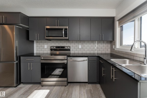 Modern kitchen with dark grey cabinets, stainless steel appliances, and white subway tile backsplash. - #40 850 Secord Bv Nw, Edmonton