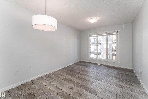 Empty dining area with light grey walls, wood plank flooring, and a large window. - #40 850 Secord Bv Nw, Edmonton