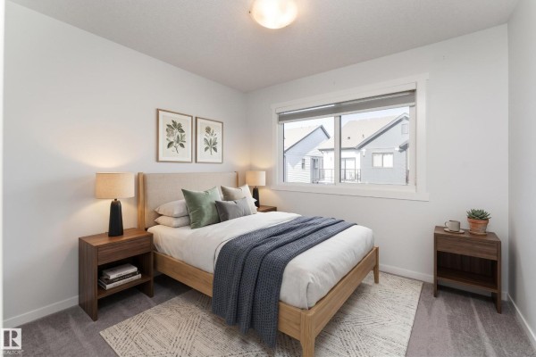 Bedroom with a queen-sized bed, wood nightstands, and a window overlooking houses. - #40 850 Secord Bv Nw, Edmonton